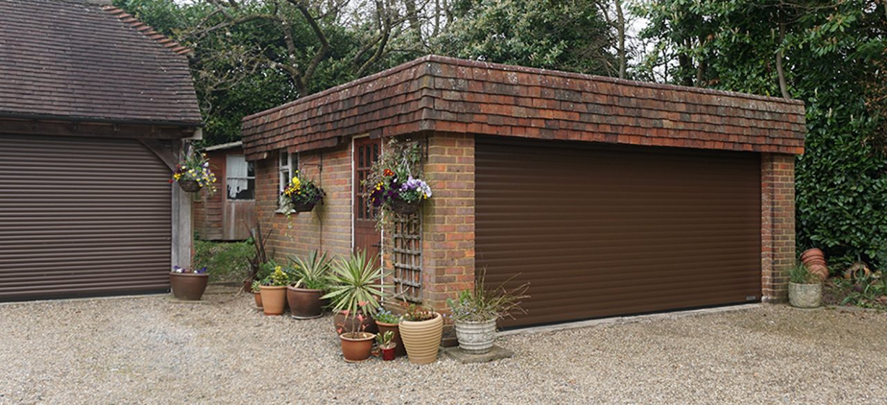 Brown up and over garage door in a stand-alone red brick garage. 